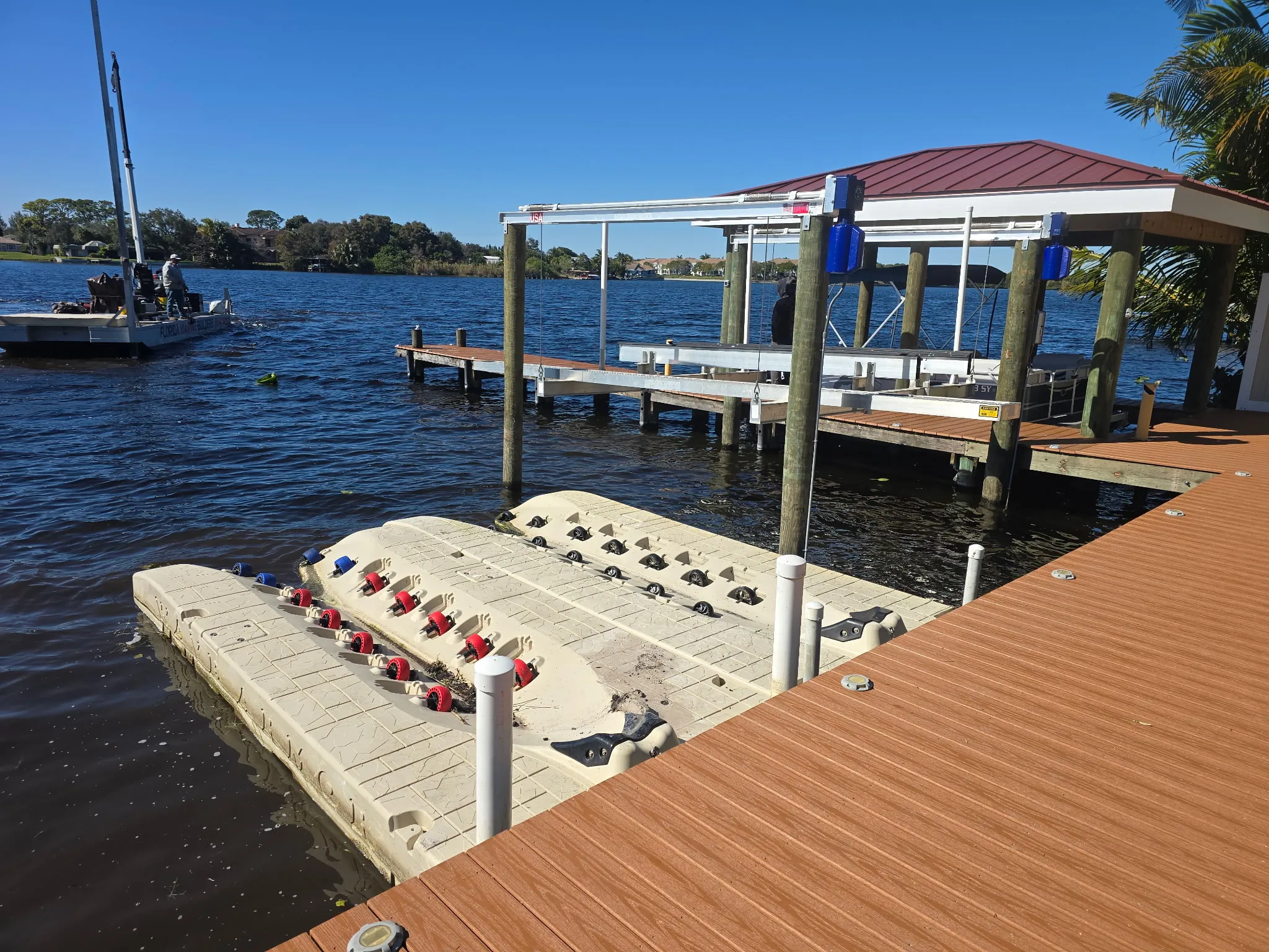 Floating drive-on dock, composite decking, and a covered boat lift built by Florida Marine Builders, with the company barge on the water behind