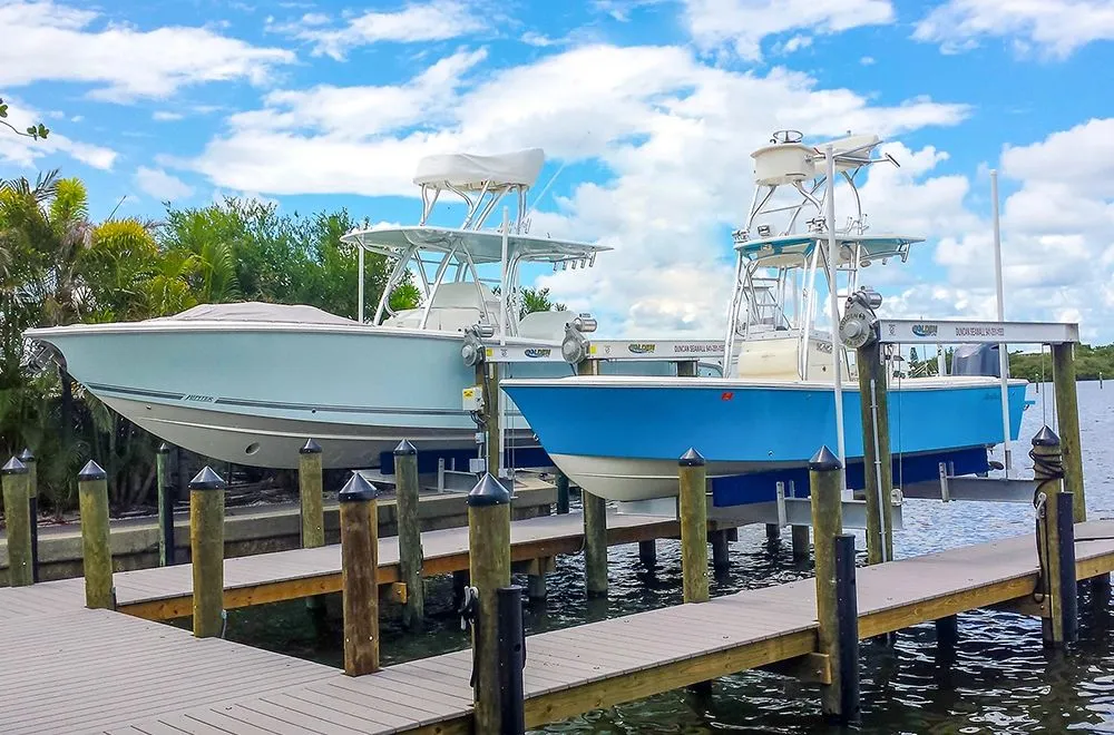 Two center-console boats raised side by side on boat lifts beside a composite dock