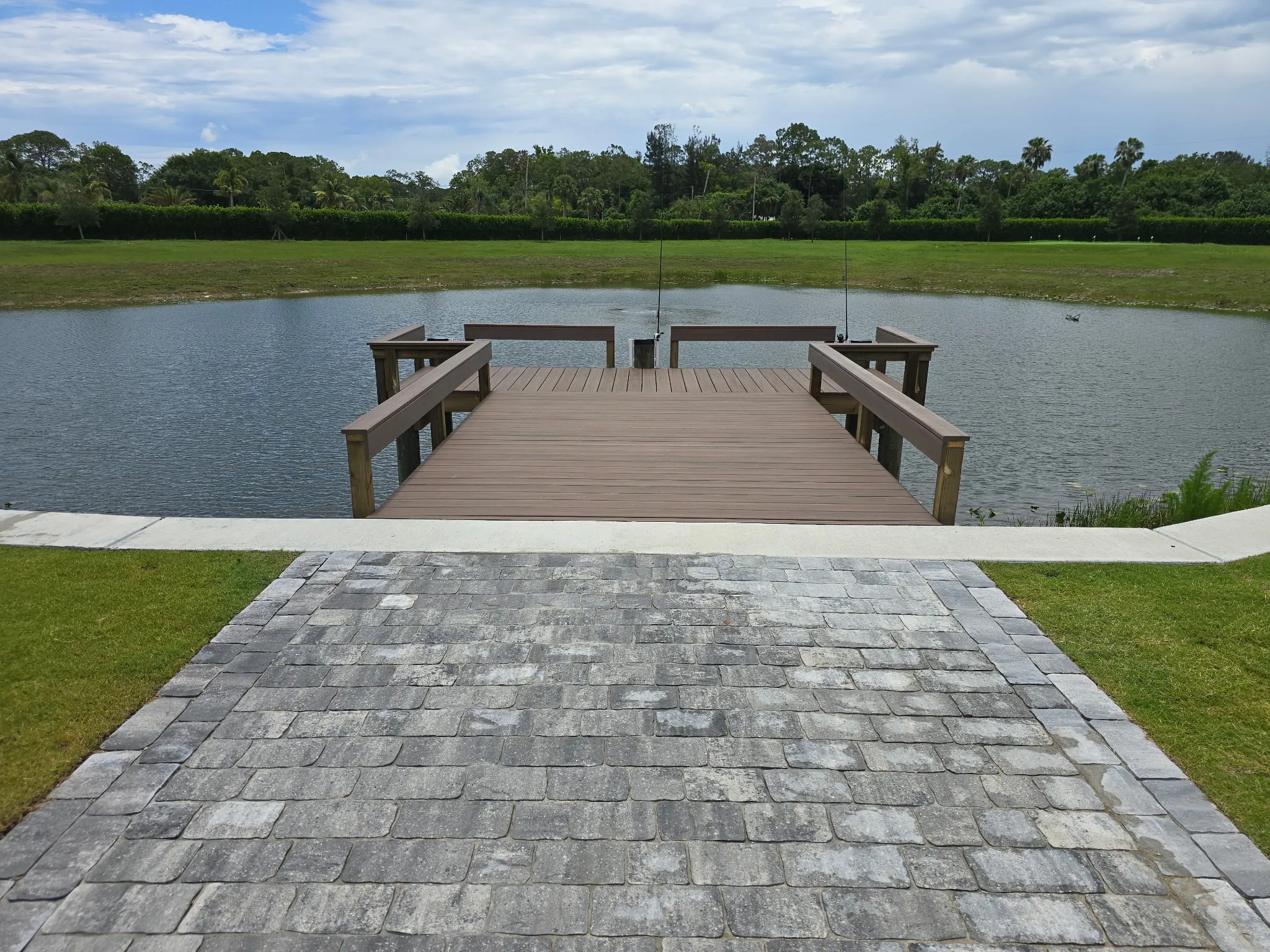 Composite fishing dock with bench rails reaching into a pond from a paver landing, built by Florida Marine Builders