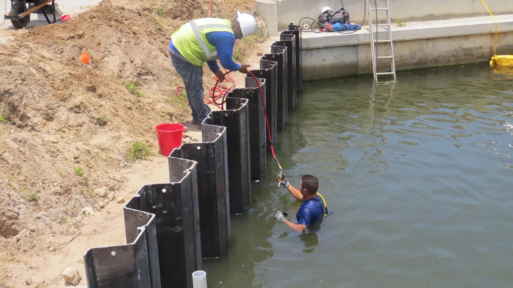 Crew installing interlocking vinyl seawall panels along a residential canal, working from land and in the water